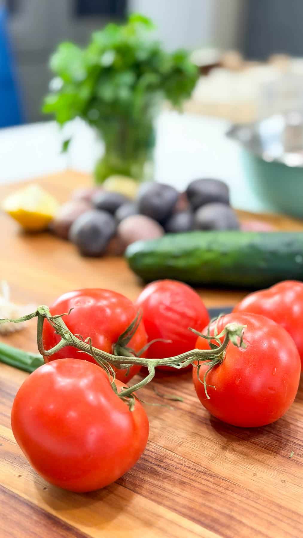 vine tomatoes on a wooden board, with cucumber, and potatoes in the background