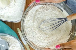 SIFTED CAKE FLOUR IN GLASS BOWLS WITH HANDS HOLDING THE SIDE OF THE BOWL