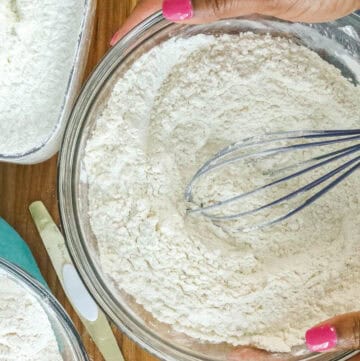 SIFTED CAKE FLOUR IN GLASS BOWLS WITH HANDS HOLDING THE SIDE OF THE BOWL