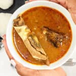 hands holding a bowl of palm nut soup
