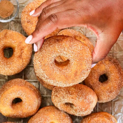 hand holding one donut on top of a bed of donuts