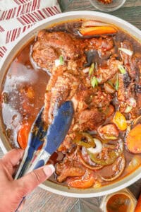 tongs lifting turkey wings from stew